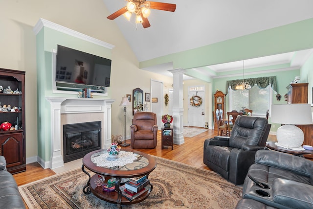 living room featuring wood finished floors, ornate columns, a tiled fireplace, ceiling fan with notable chandelier, and vaulted ceiling
