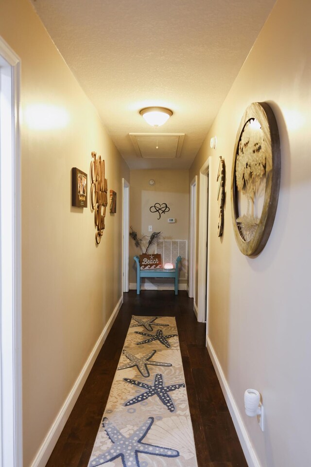 corridor with attic access, baseboards, and dark wood-style flooring