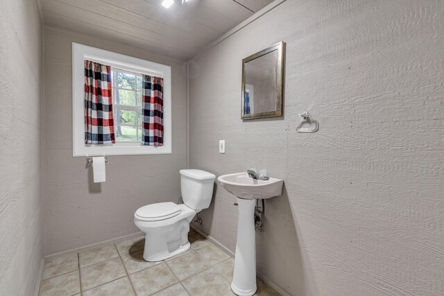 half bath with a sink, toilet, tile patterned flooring, and baseboards