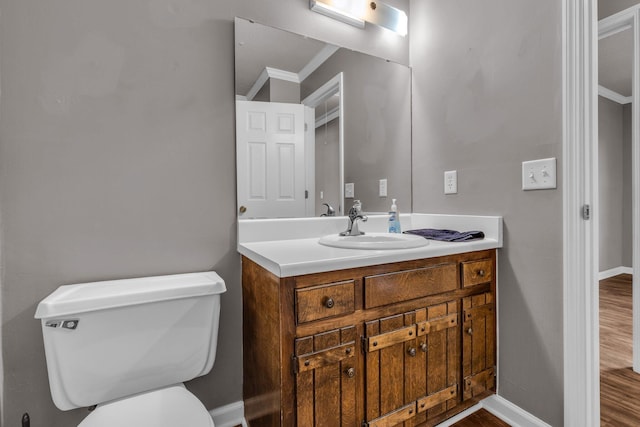 bathroom with baseboards, toilet, ornamental molding, wood finished floors, and vanity