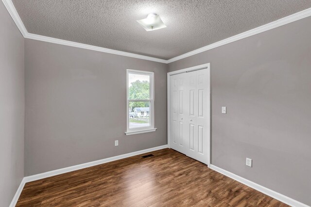 unfurnished bedroom with wood finished floors, a closet, ornamental molding, baseboards, and a textured ceiling