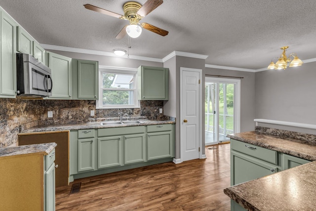kitchen with stainless steel microwave, a sink, green cabinets, dark wood-type flooring, and a textured ceiling