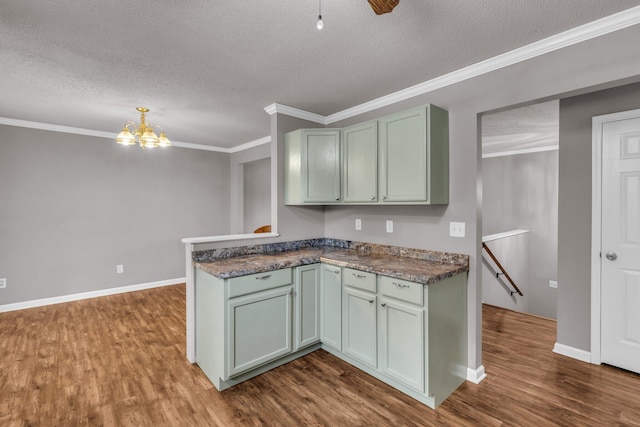 kitchen with a textured ceiling, crown molding, an inviting chandelier, dark wood-style flooring, and a peninsula