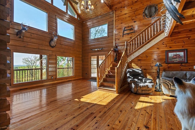 living room featuring high vaulted ceiling, hardwood / wood-style floors, wood walls, stairs, and a notable chandelier