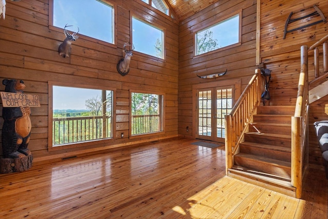 unfurnished living room featuring high vaulted ceiling, a wealth of natural light, stairway, and wood walls