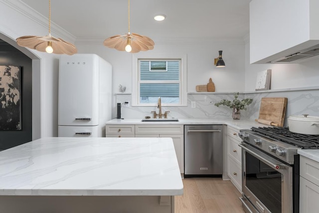 kitchen with appliances with stainless steel finishes, tasteful backsplash, a sink, light stone counters, and light wood-style floors