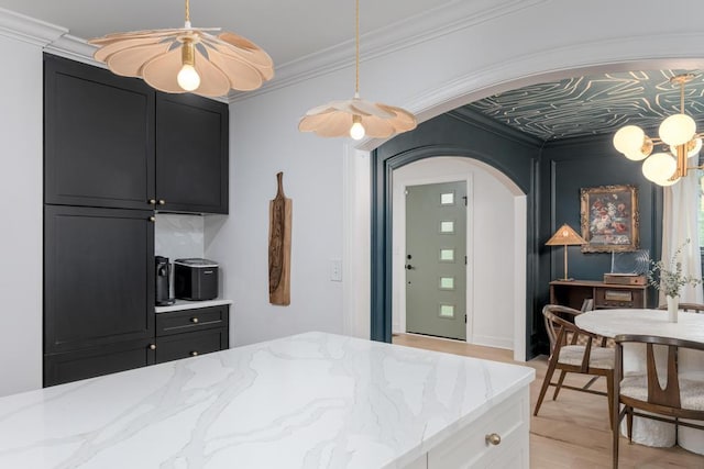 interior space with dark cabinetry, arched walkways, crown molding, and light wood-style floors