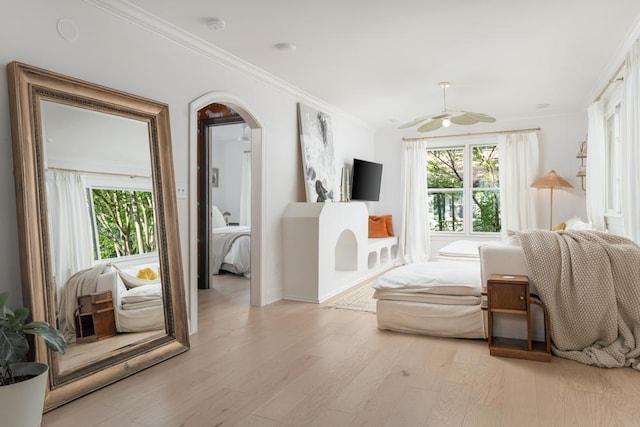 bedroom featuring crown molding, a ceiling fan, baseboards, arched walkways, and light wood-style flooring