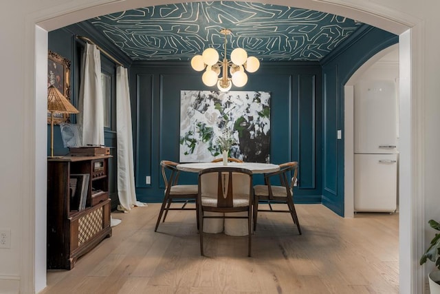 dining space with arched walkways, light wood-type flooring, an ornate ceiling, a notable chandelier, and a decorative wall
