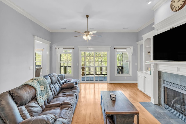 living area featuring a tile fireplace, light wood-style flooring, a ceiling fan, and crown molding