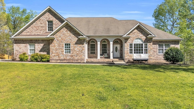 view of front of home with brick siding, a front lawn, a shingled roof, and a porch