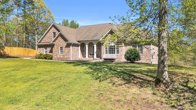 view of front of home with a front yard, fence, brick siding, and a shingled roof