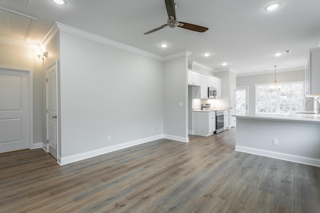 unfurnished living room with crown molding, ceiling fan with notable chandelier, attic access, and recessed lighting