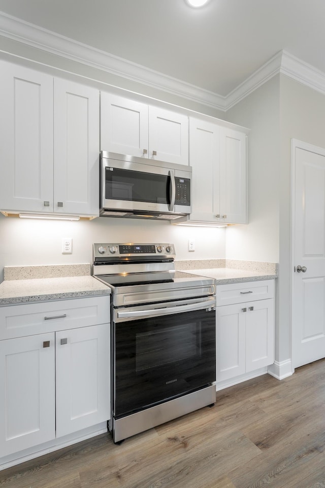 kitchen featuring light wood-type flooring, light stone counters, crown molding, white cabinets, and appliances with stainless steel finishes