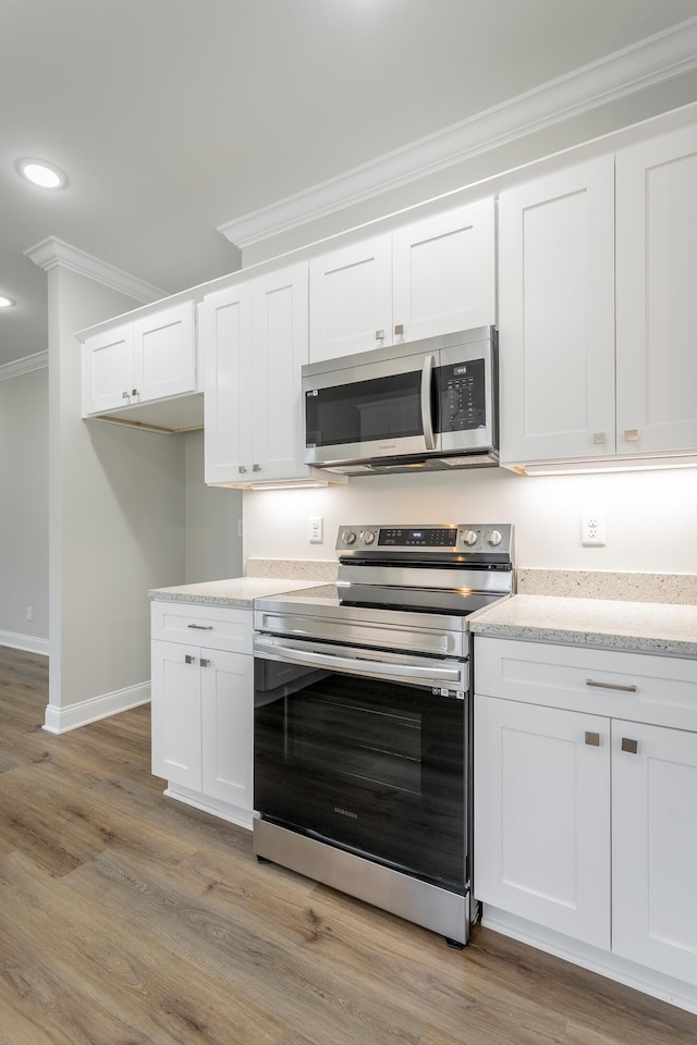 kitchen featuring baseboards, crown molding, white cabinetry, recessed lighting, and stainless steel appliances