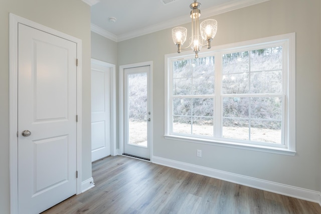 unfurnished dining area with baseboards, a notable chandelier, a healthy amount of sunlight, crown molding, and wood finished floors