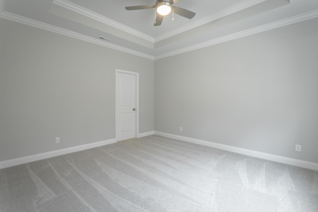 empty room with a tray ceiling, light carpet, ceiling fan, and crown molding