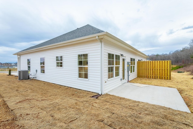 back of property with a patio, roof with shingles, central air condition unit, and fence