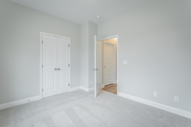 unfurnished bedroom with a closet, light colored carpet, and baseboards