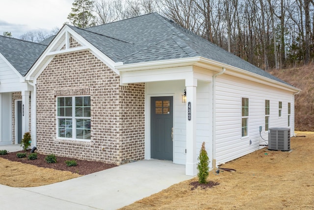 view of front of house with central AC, a shingled roof, and brick siding