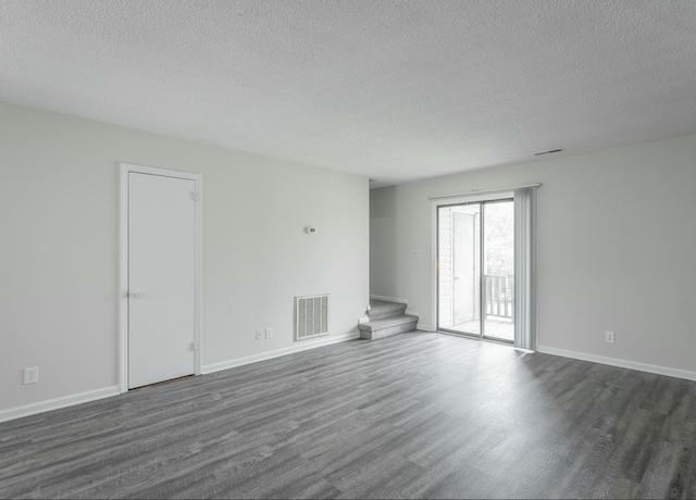 unfurnished room with visible vents, dark wood-style floors, a textured ceiling, and stairs