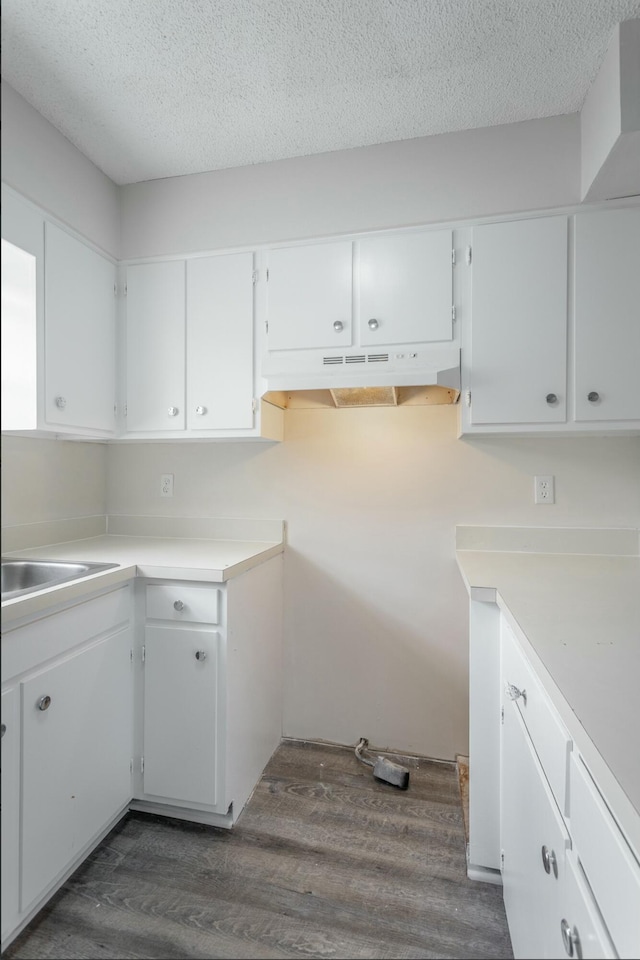 kitchen with dark wood-style floors, under cabinet range hood, light countertops, a textured ceiling, and white cabinetry