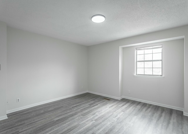 spare room featuring baseboards, dark wood-style flooring, and a textured ceiling