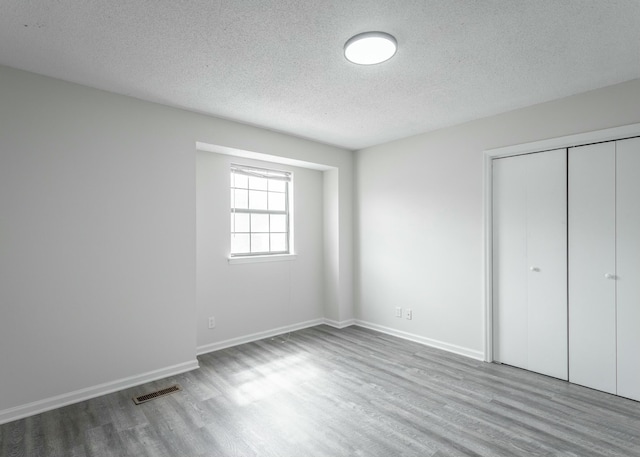 unfurnished bedroom with a closet, wood finished floors, visible vents, and a textured ceiling
