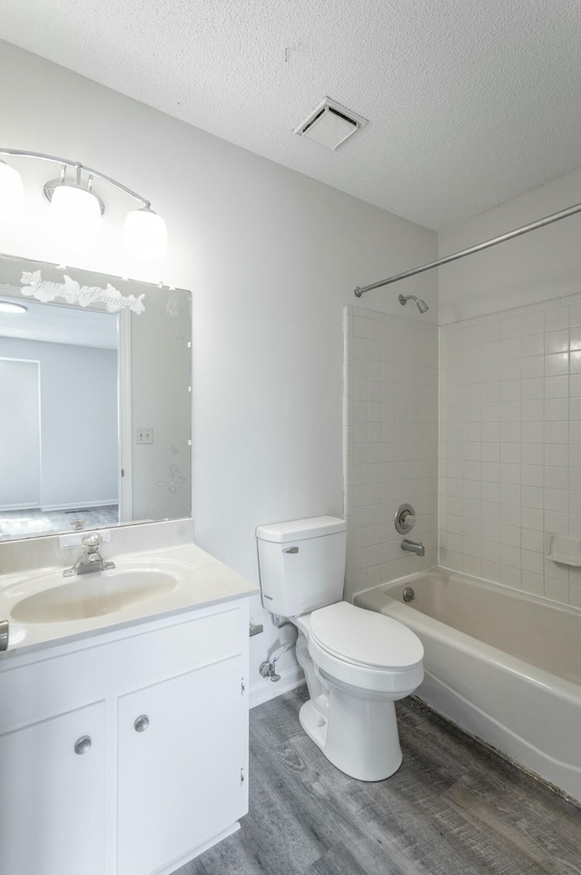 full bath featuring wood finished floors, a textured ceiling, vanity, toilet, and visible vents