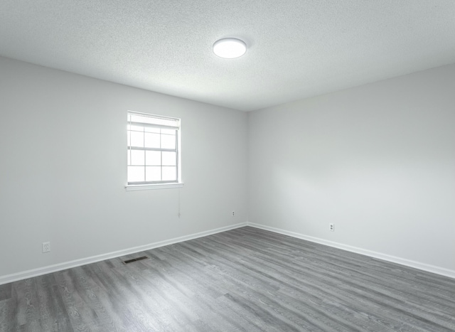 empty room with baseboards, visible vents, a textured ceiling, and dark wood-type flooring