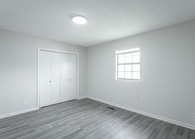 unfurnished bedroom with a textured ceiling, a closet, dark wood finished floors, baseboards, and visible vents