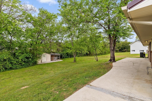 view of yard with driveway, an outdoor structure, central AC, and a patio area