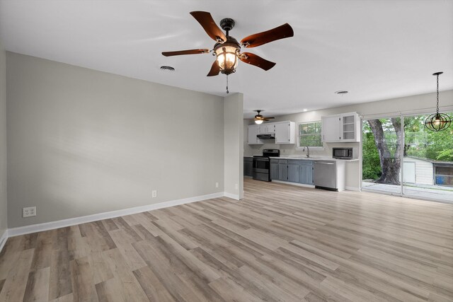 unfurnished living room featuring a sink, light wood-style floors, visible vents, baseboards, and ceiling fan with notable chandelier