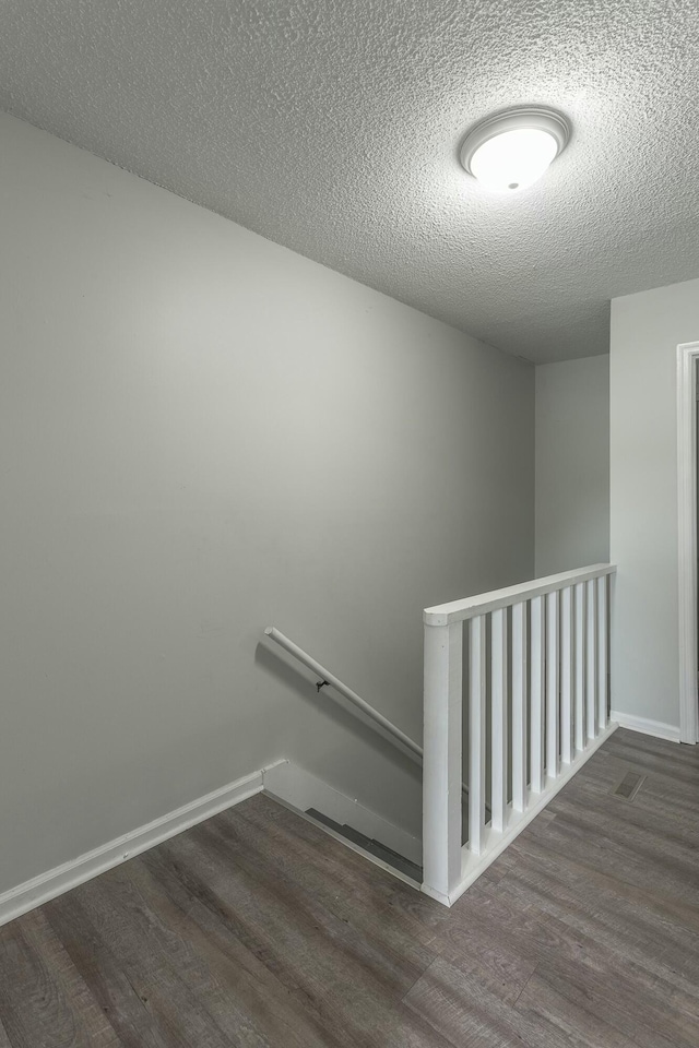 stairway with wood finished floors, a textured ceiling, and baseboards