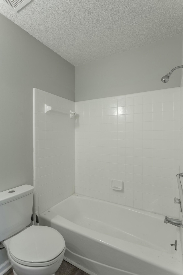 bathroom with toilet, a textured ceiling, and bathing tub / shower combination