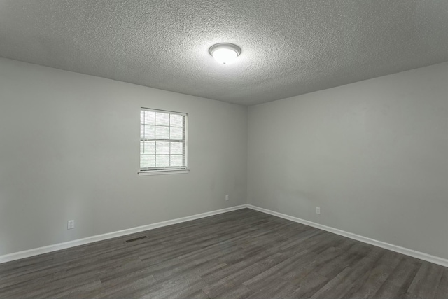 spare room with a textured ceiling, baseboards, visible vents, and dark wood-style floors