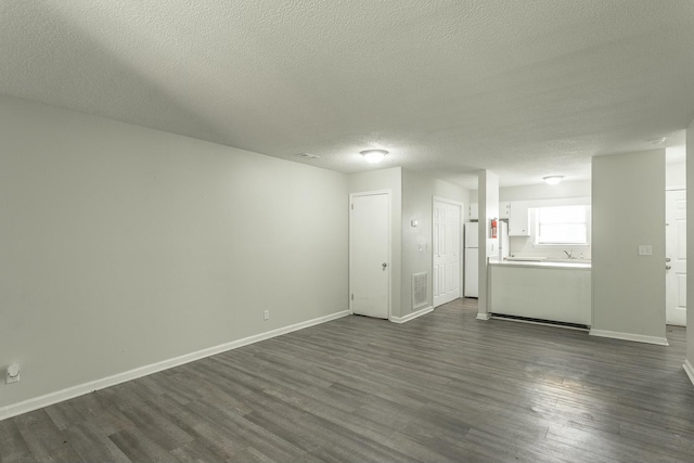 unfurnished living room with visible vents, baseboards, a textured ceiling, and dark wood-style flooring