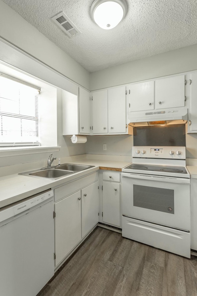 kitchen with a sink, a textured ceiling, visible vents, white appliances, and under cabinet range hood