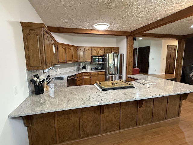 kitchen featuring stainless steel appliances, backsplash, a sink, beam ceiling, and a peninsula