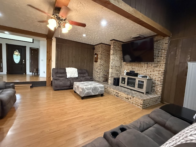 living room featuring wood walls, wood finished floors, ceiling fan, and a textured ceiling