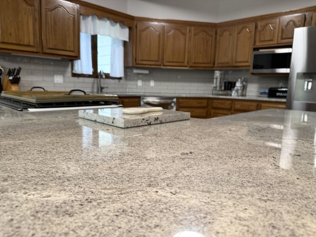 kitchen featuring light stone countertops, stainless steel appliances, decorative backsplash, and brown cabinetry