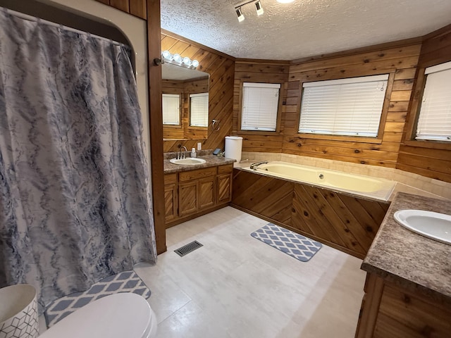 bathroom with wood walls, a bath, vanity, visible vents, and a textured ceiling