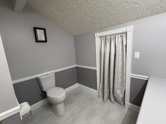bathroom with baseboards, toilet, a textured ceiling, and vaulted ceiling