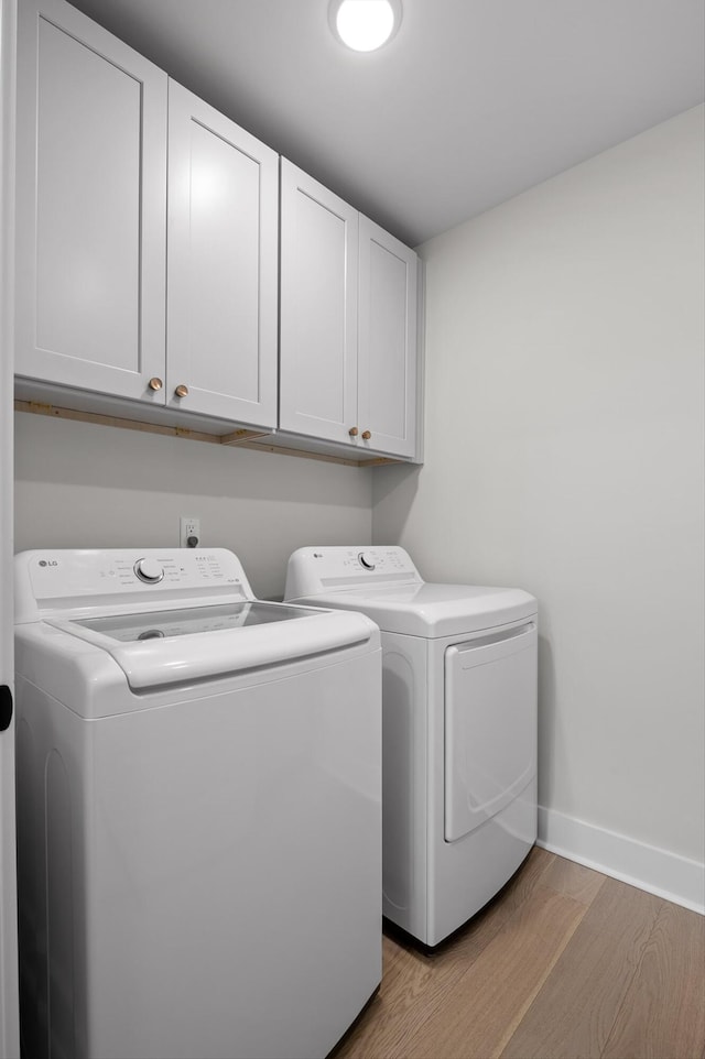 washroom with baseboards, light wood-style flooring, washing machine and dryer, and cabinet space