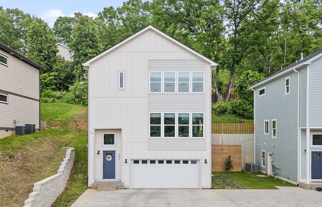 view of front facade with board and batten siding, central AC unit, a garage, fence, and concrete driveway