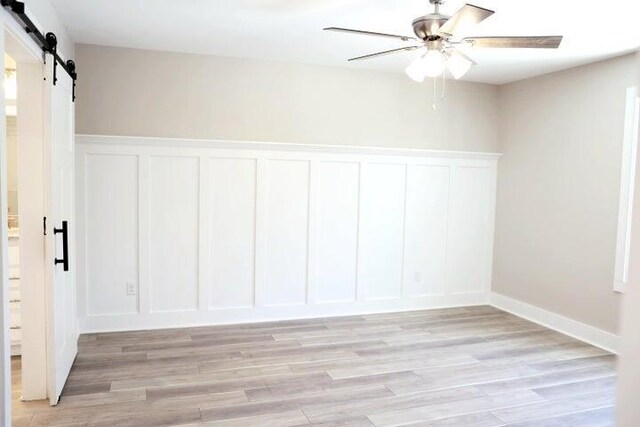 unfurnished room featuring wainscoting, a barn door, a decorative wall, and light wood-type flooring