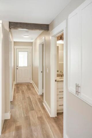 hall with light wood finished floors, baseboards, and beam ceiling