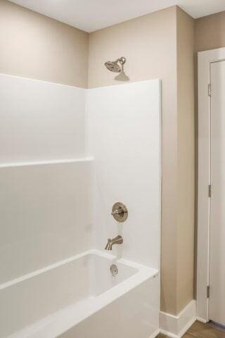 bathroom featuring baseboards, wood finished floors, and washtub / shower combination