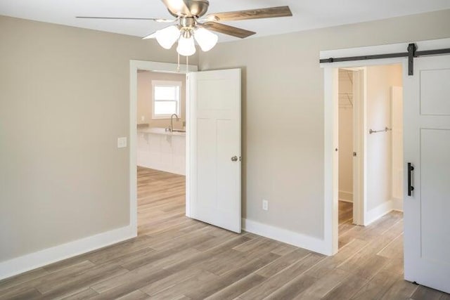 unfurnished room with a barn door, wood finished floors, a sink, baseboards, and ceiling fan