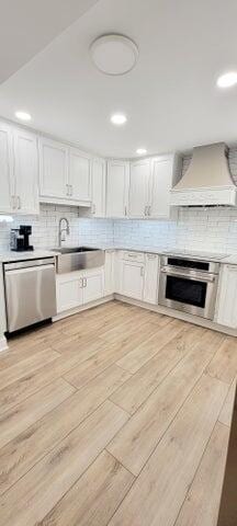 kitchen with premium range hood, backsplash, light wood-type flooring, and stainless steel appliances